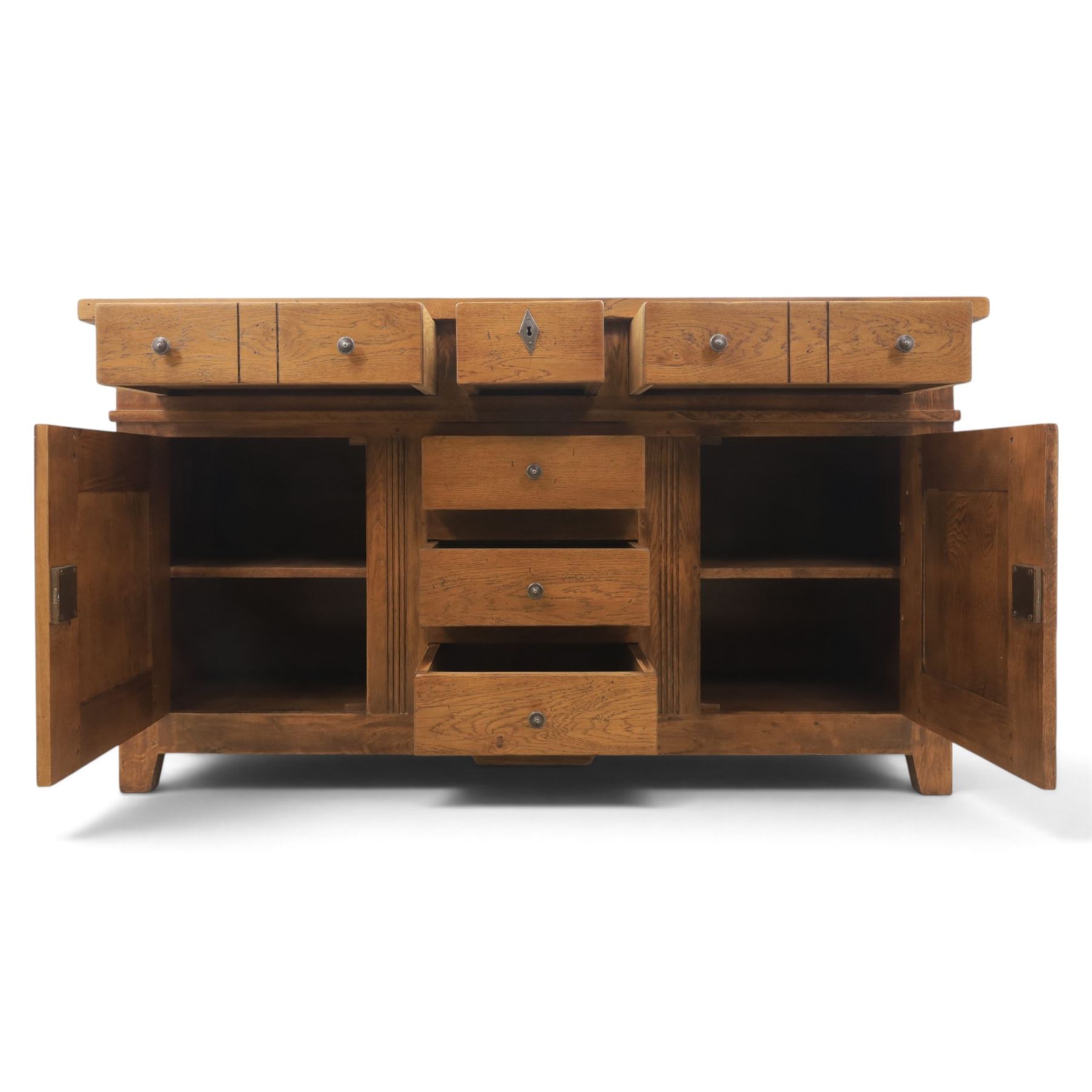 Indigo Furniture - large rustic oak sideboard fitted, with three drawers above three central drawers, flanked by fielded panelled doors, raised on bracket feet
