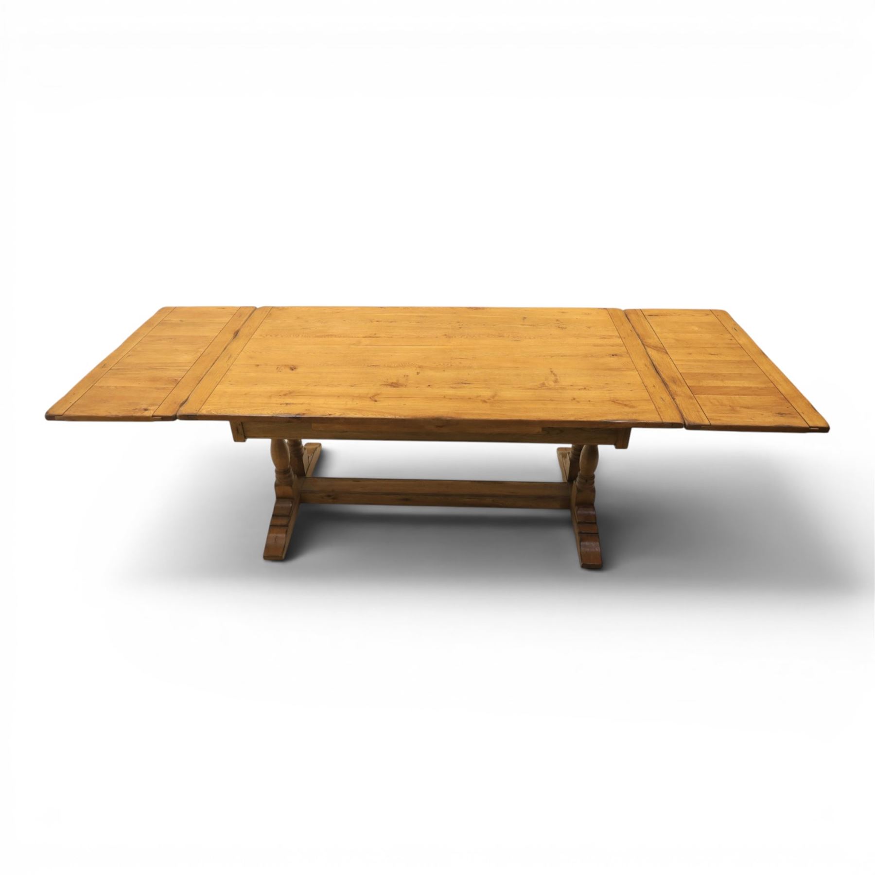 Traditional oak refectory dining table, fitted with draw leaves to either end extending to 257cm, on twin turned and block supports united by a stretcher, terminating in shaped trestle feet