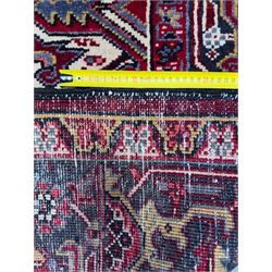 Northwestern Persian Heriz carpet, the madder red field centred by a large octofoil medallion with serrated edge, flanked by ivory stepped spandrels and geometric floral motifs in indigo, ochre and sky blue, enclosed by a navy border of rosettes and angular vines, from the region of Heriz