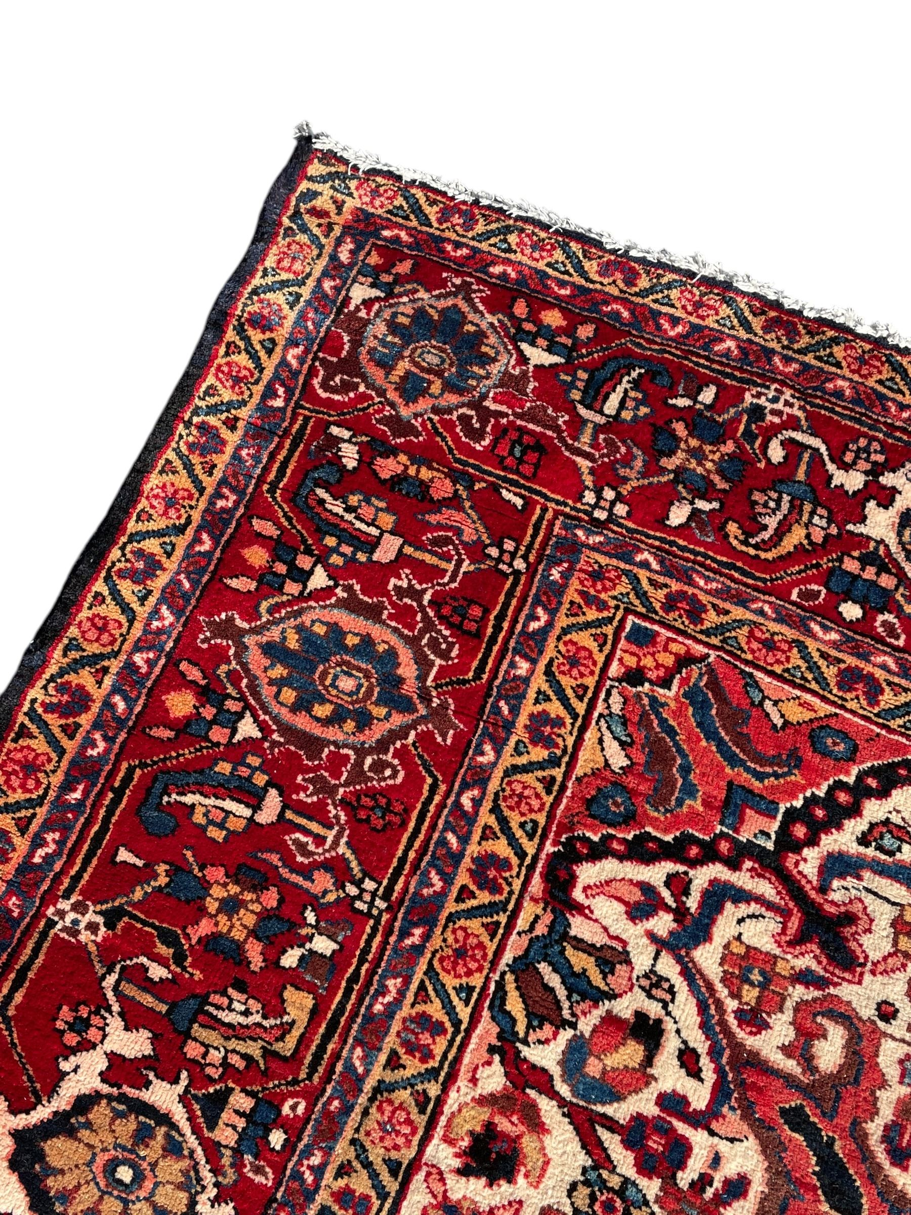 Persian Hamadan indigo and red ground carpet, large central medallion decorated with projecting palmette motifs, the surrounding field decorated with trailing branches and flower heads, crimson ground border decorated with stylised plant motifs, within floral pattern guard stripes 