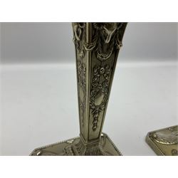 Pair of late Victorian silver plated Adam style candlesticks, each with square base with canted corners and beaded edge, repousse decorated with urns an stiff leaves, leading to a tapering column decorated with rams heads, husk swags, and garlands, supporting a urn shaped sconce with conforming decoration and removable nozzle with beaded edge, H31.5cm