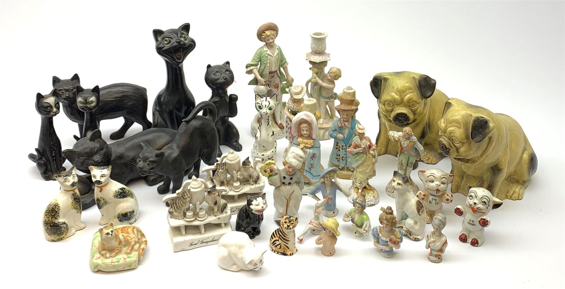 A collection of various ceramic figurines, to include pair of small 19th century Staffordshire cats, Royal Doulton cat, Coalport cat, pair of 19th century pug dogs, two fairings inscribed Good Templars, two Bonzo dog peppers, a number of pin cushion dolls, various 20th century and later black pottery cats, Victorian bisque figures, etc. 