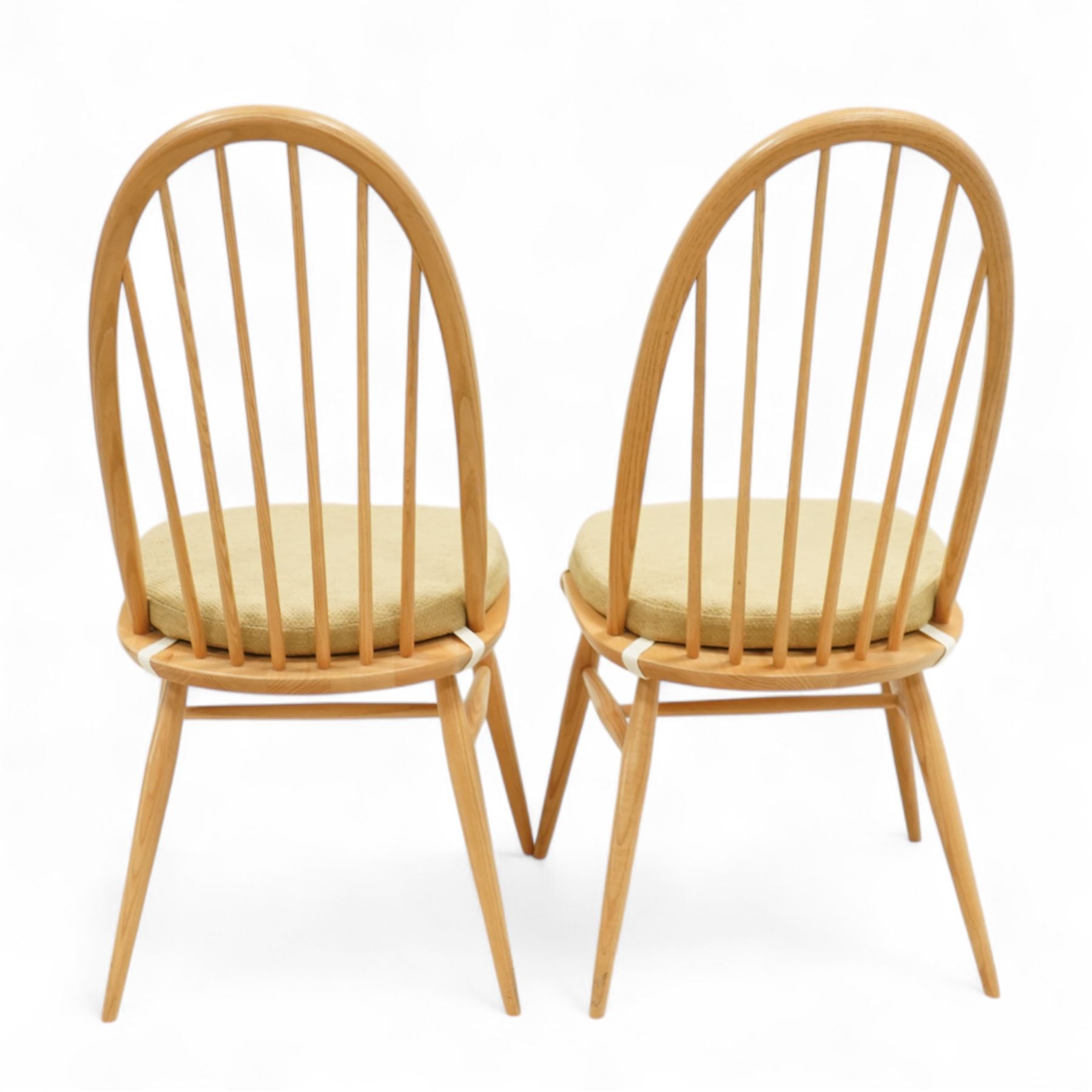 Ercol - light elm set of four Quaker style chairs, high arched backrest with slender spindles, solid wood seat with elasticated strap cushion, on round tapered out swept legs (4)