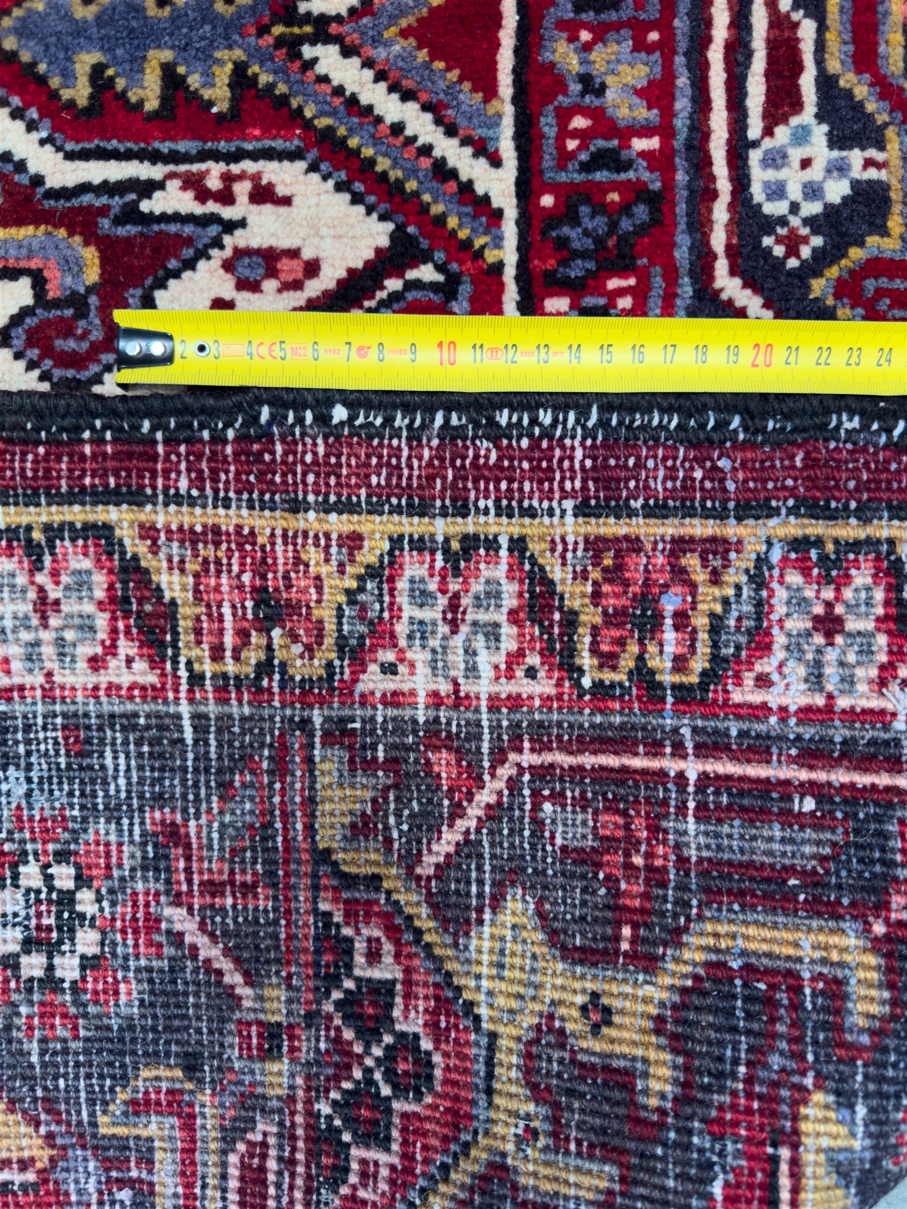 Northwestern Persian Heriz carpet, the madder red field centred by a large octofoil medallion with serrated edge, flanked by ivory stepped spandrels and geometric floral motifs in indigo, ochre and sky blue, enclosed by a navy border of rosettes and angular vines, from the region of Heriz