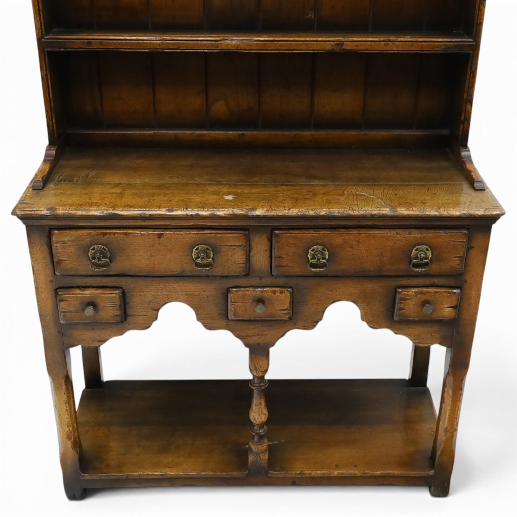 Georgian design oak dresser of small proportions, moulded cornice over open plate rack with two shelves and shaped apron, the base fitted with two drawers over three small drawers, brass drop handles, shaped apron, on square supports united by pot board