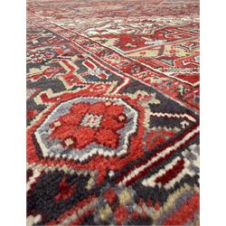 Northwestern Persian Heriz carpet, the madder red field centred by a large octofoil medallion with serrated edge, flanked by ivory stepped spandrels and geometric floral motifs in indigo, ochre and sky blue, enclosed by a navy border of rosettes and angular vines, from the region of Heriz