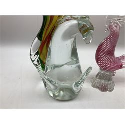Three Murano style glass cockatoo parrots, the first with mottled yellow, red and orange body, clear outstretched wings, dark blue beak and red crest, raised upon clear stylised base, the second smaller parrot with merging blue and green body, and further with pink striped body, tallest H40cm