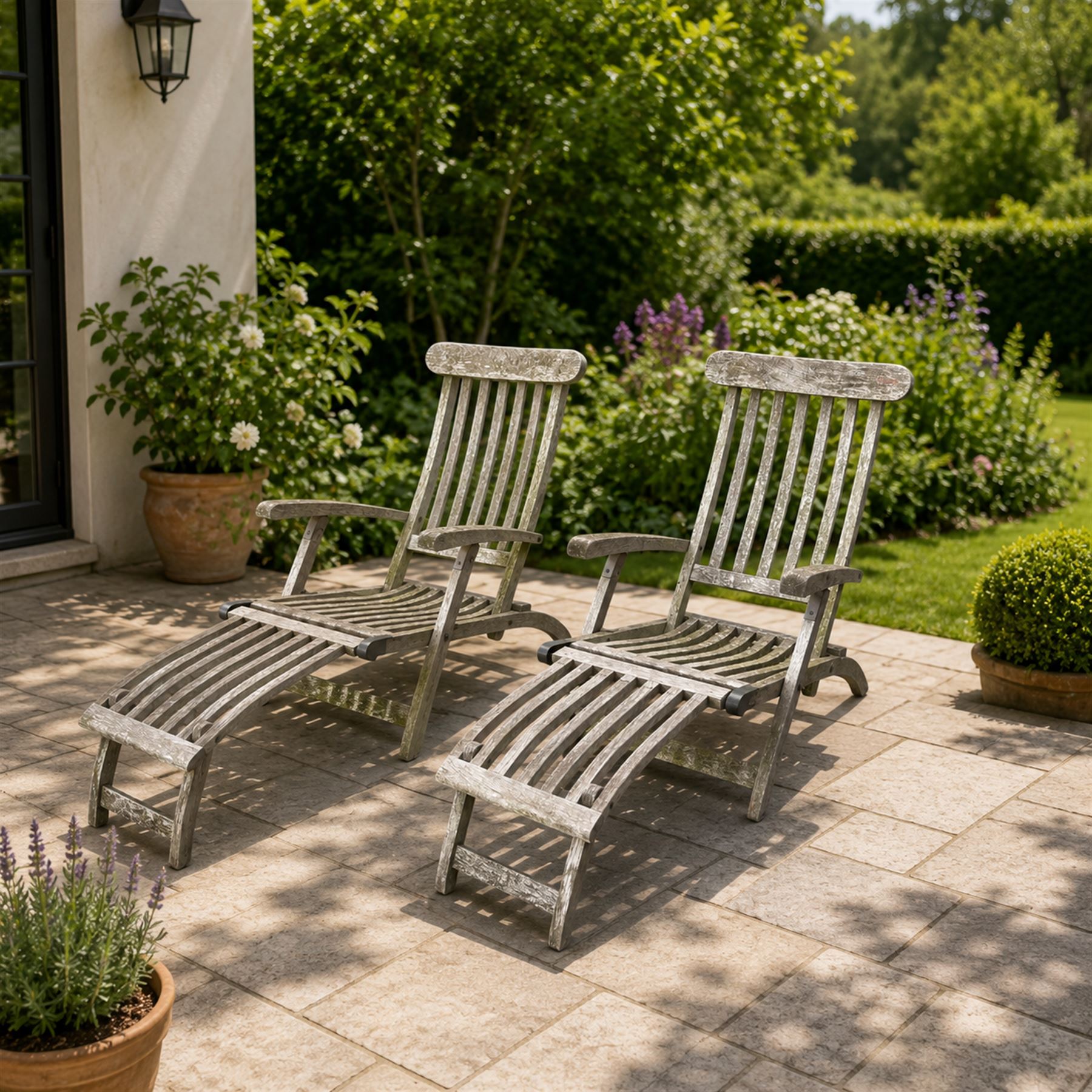 Pair of teak reclining garden steamer armchairs, each with an adjustable slatted back, curved slatted seat and footstool