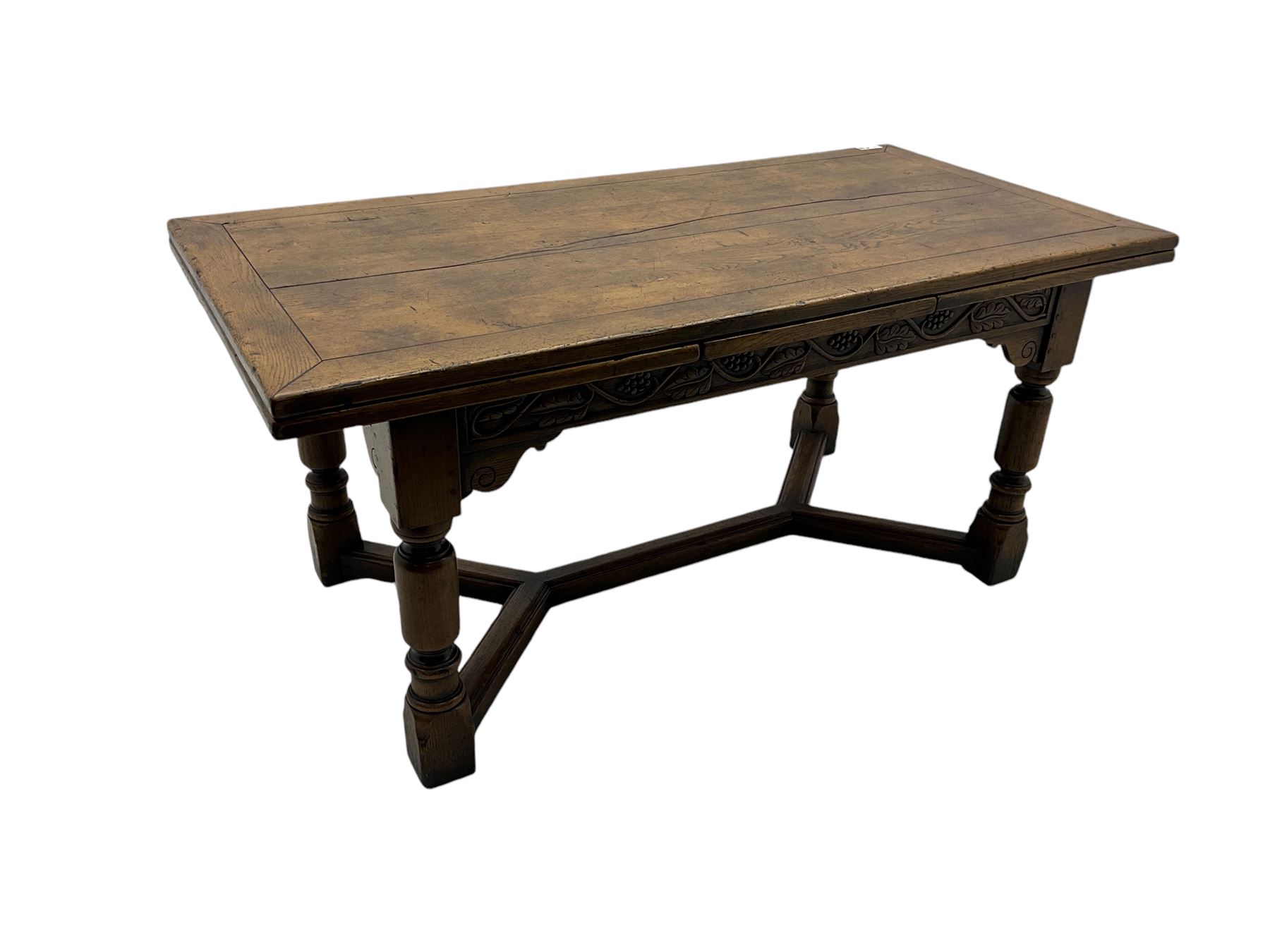 Early 20th century Jacobean design draw-leaf oak dining table, rectangular top with carved frieze depicting scrolling foliage and grape clusters, sliding extending leaves, raised on robust turned supports united by H-stretcher  