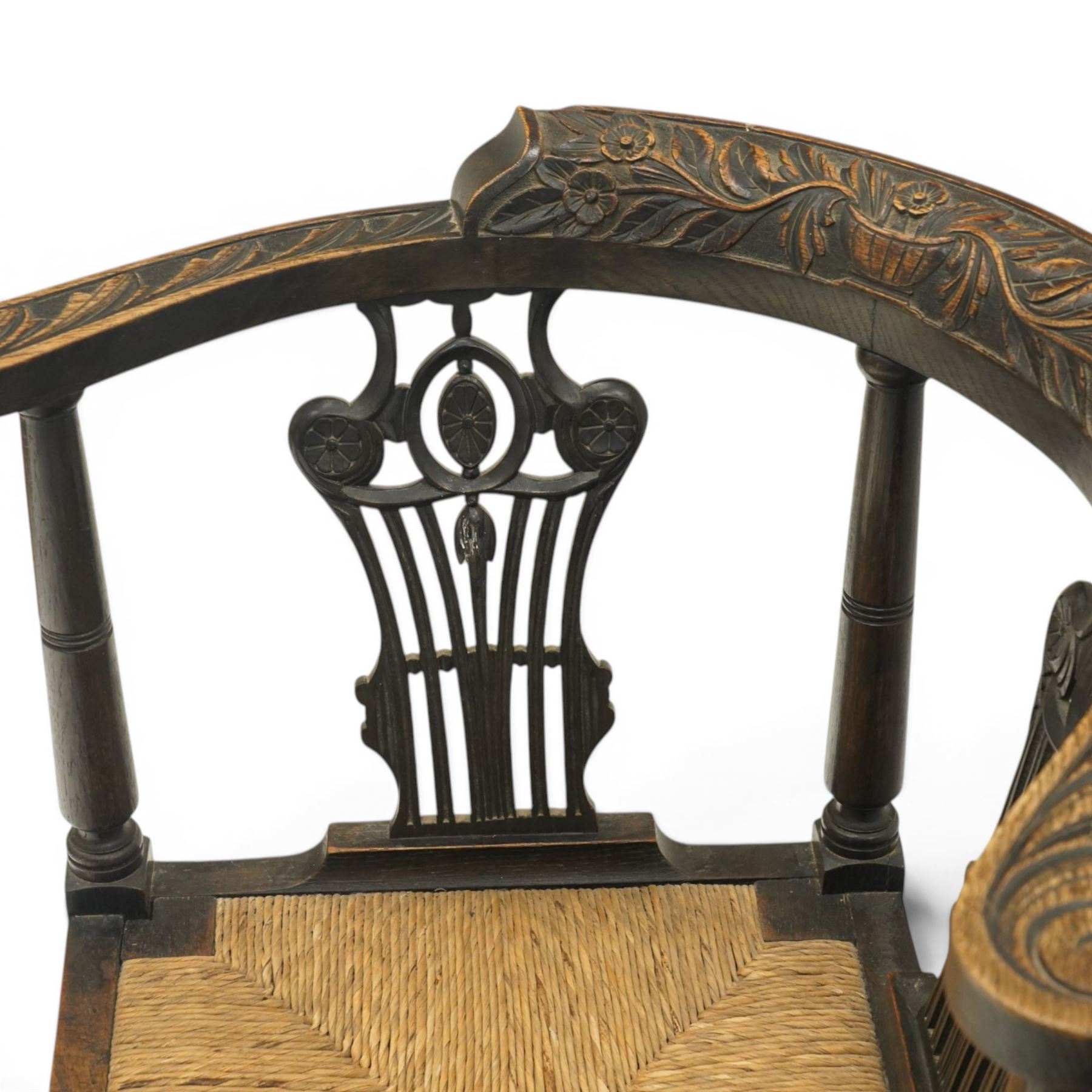 Pair of 19th century carved oak corner chairs, cresting rail carved with central floral bouquet with trailing foliage extending to the scroll arm terminals, pierced back splats with rosette motifs over drop-in rush seats, front cabriole support with acanthus carved knee and ball-and-claw foot