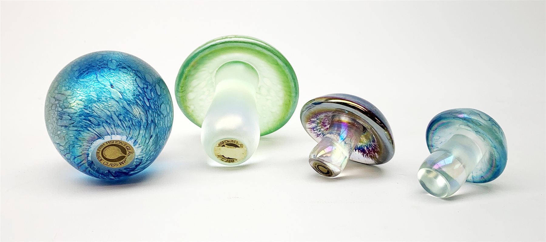 Three John Ditchfield Glasform iridescent mushroom paperweights, two with paper labels beneath, largest H9cm, together with a John Ditchfield Glasform apple paperweight, in iridescent blue, with paper label beneath. 