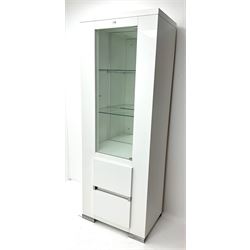 Gloss white illuminated display cabinet, single door enclosing two glazed shelves above cupboard on metal supports 