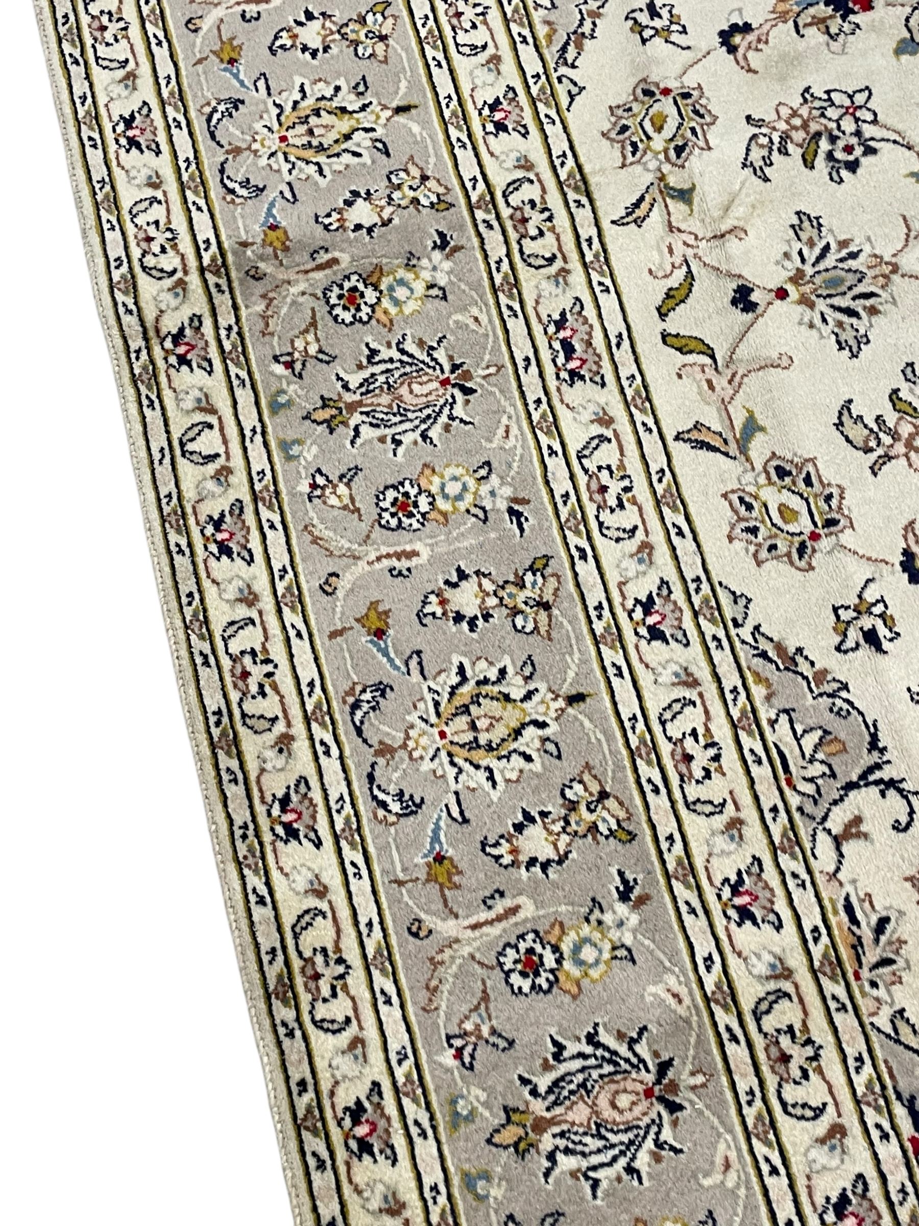 Persian Kashan ivory ground carpet, floral central medallion surrounded by trailing leafy branches and palmettes, floral pattern spandrels and matching border, within guard stripes
