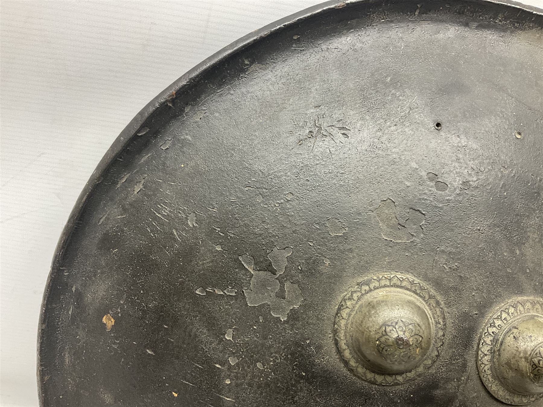 Indian black lacquered hide shield/dhal, of circular convex form with strongly outward-turned brim, fitted at its centre with four metal bosses, each of hemispherical form, with traces of silvered foliate decoration, the bosses corresponding on the inside with four iron rings for enarmes D49cm