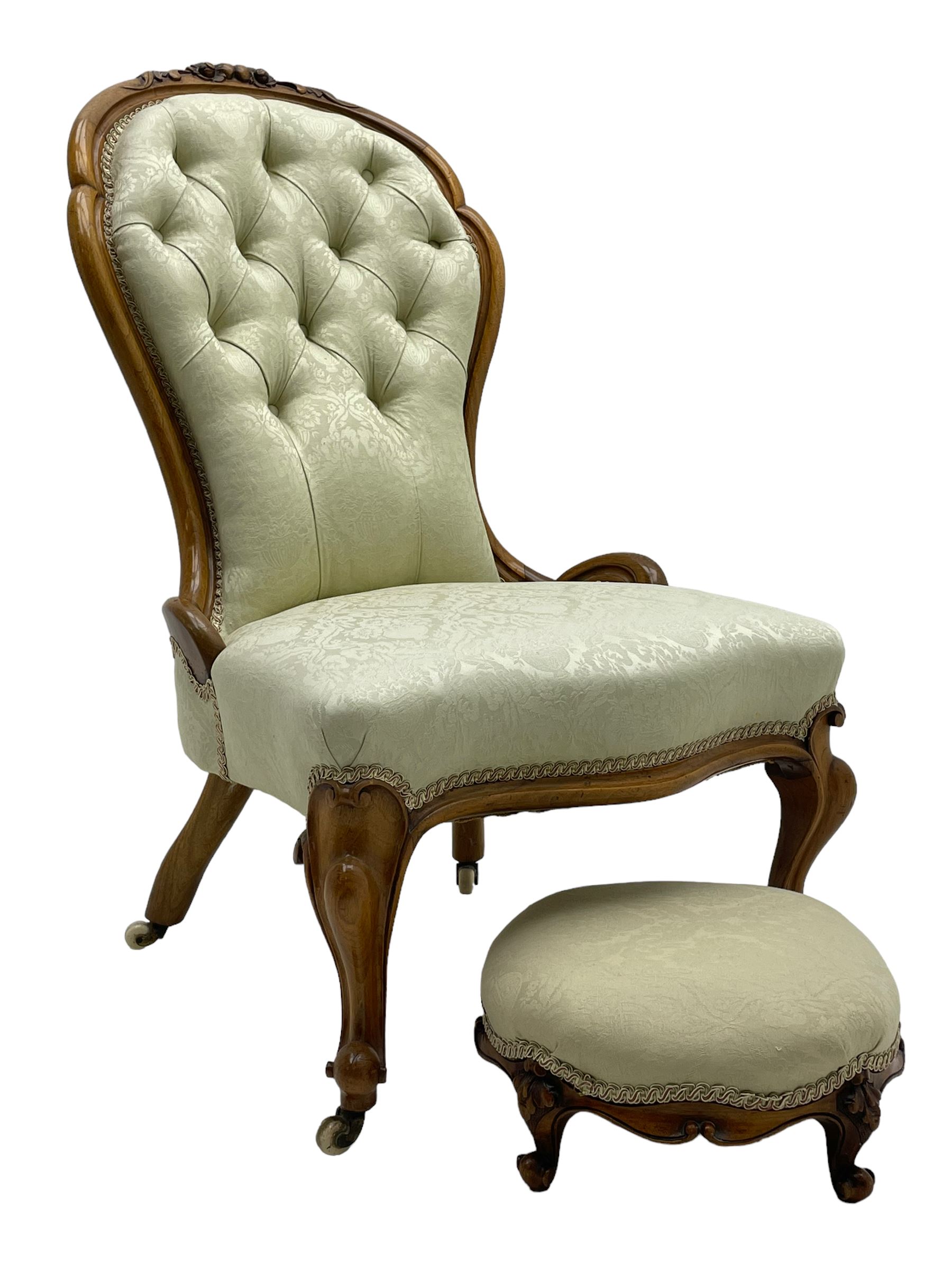 Victorian walnut framed nursing chair, the cresting rail decorated with carved applied flower heads and acanthus leaves, shaped back and sprung seat upholstered in buttoned ivory damask fabric, serpentine front over cartouche carved cabriole supports with ceramic castors (W57cm H92cm); with matched footstool, circular top over shaped moulded apron, on floral carved cabriole feet (W34cm) 