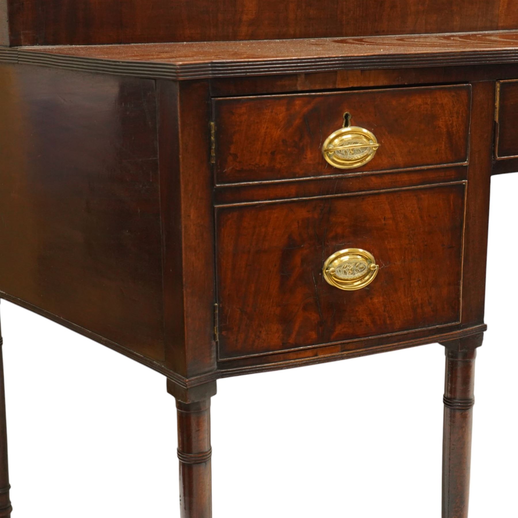 Large George III mahogany bowfront sideboard, the shaped top with raised superstructure fitted with three compartments with hinged tops and reeded edge, the body fitted with two central cock-beaded frieze drawers, flanked by a cellarette drawer and hinged cupboard both with faux double drawer facias, raised on ring turned tapering supports
Provenance: Kirkham Hall