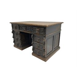 Late 19th century Gothic revival carved oak twin pedestal desk, rectangular top with inset writing surface and carved edges, central frieze drawer flanked by eight drawers, all with green man carved handles and extending trailing foliage, carvings of pineapple and lion mask corbels, the pedestals with panelled sides and back, on plinth bases