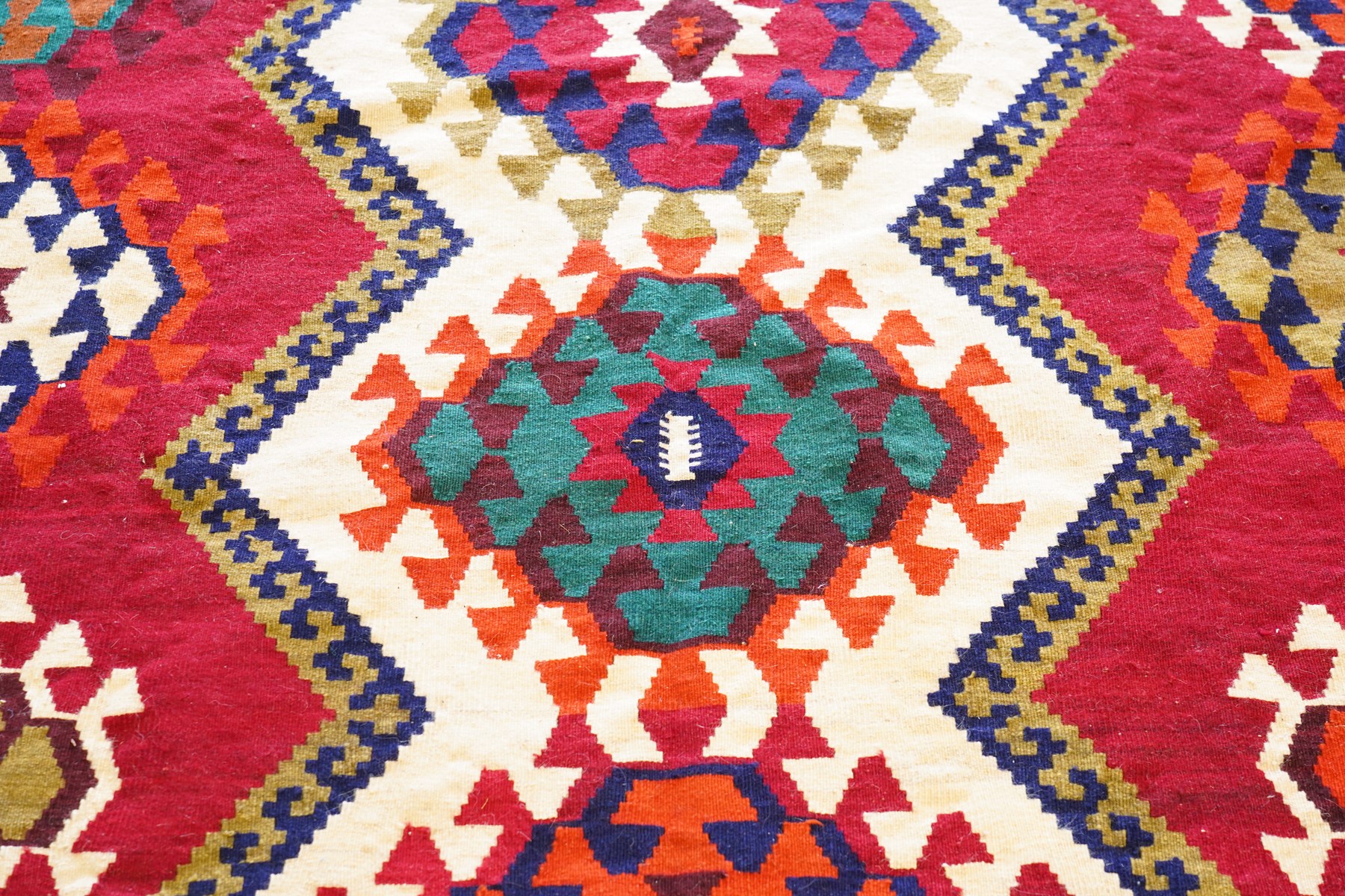 Persian Qashqai crimson ground rug, the central narrow ivory field decorated with repeating hooked geometric lozenges in multicolours, with a densely decorated guard band