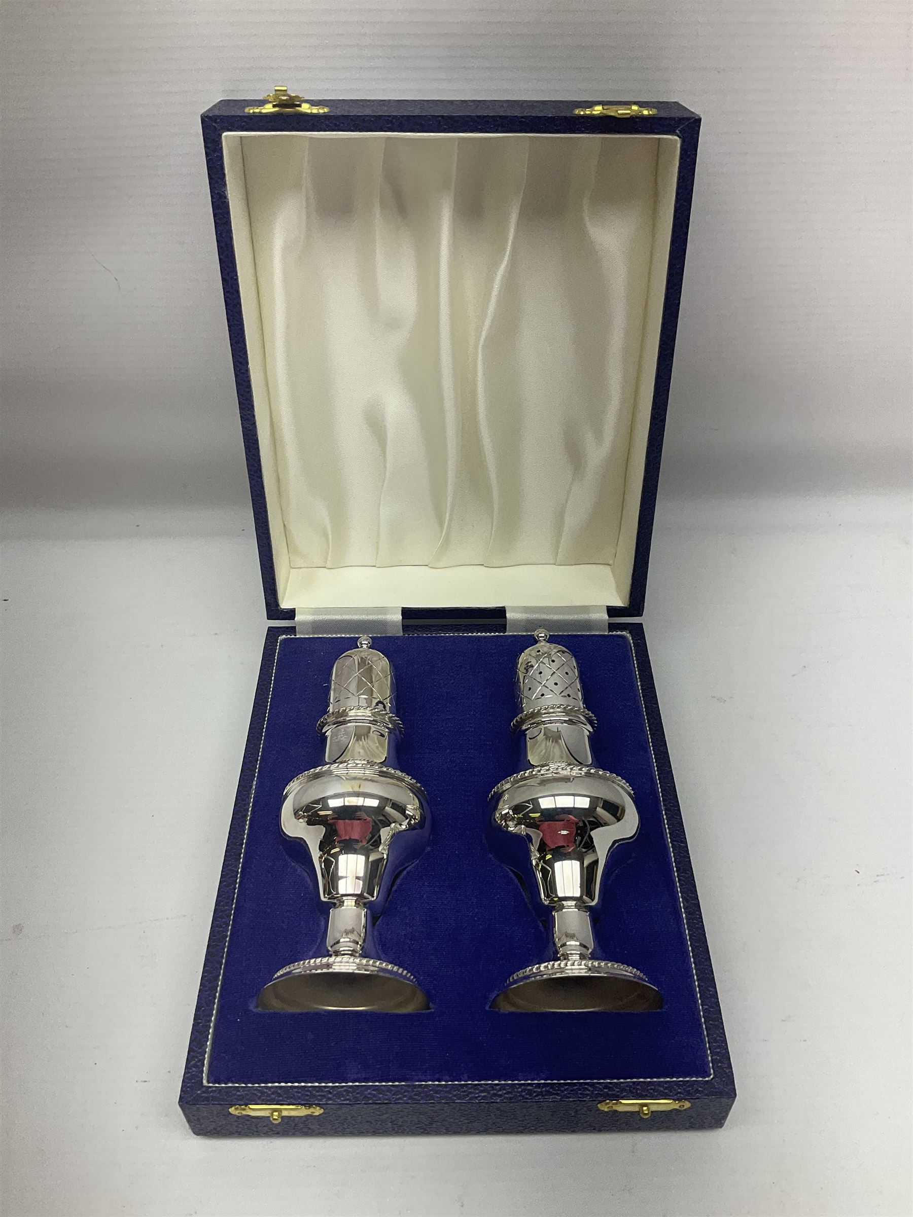 Silver plated two piece cruet set, comprising salt shaker and pepper shaker, both of waisted form with engraved rope twist borders, the removable pierced covers each with engraved lattice decoration, upon a circular spreading foot, H13.3cm, contained within velvet lined fitted case