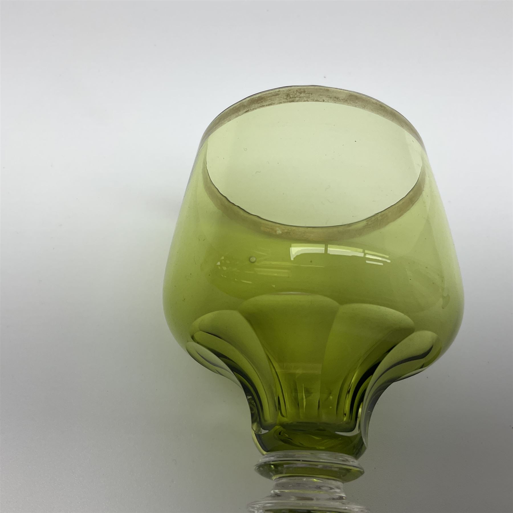 19th Century Bohemian amethyst glass lidded goblet, the bowl of faceted form, gilded with three children in period dress playing games, upon a knopped stem and conforming faceted foot, together with an art nouveau green glass goblet, with gilded rim, upon clear trumpet stem, and a hand blown wine glass, transfer printed with birds and three figures in period dress, tallest H29cm