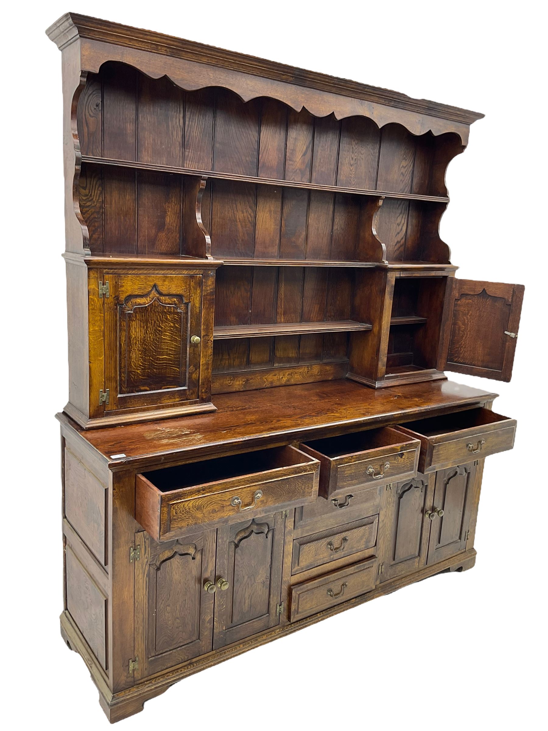 Traditional oak dresser, the moulded cornice over shaped apron, three heights plate rack fitted with two cupboards, the base fitted with six drawers and two double cupboards, panelled pointed ogee arched doors, on bracket feet