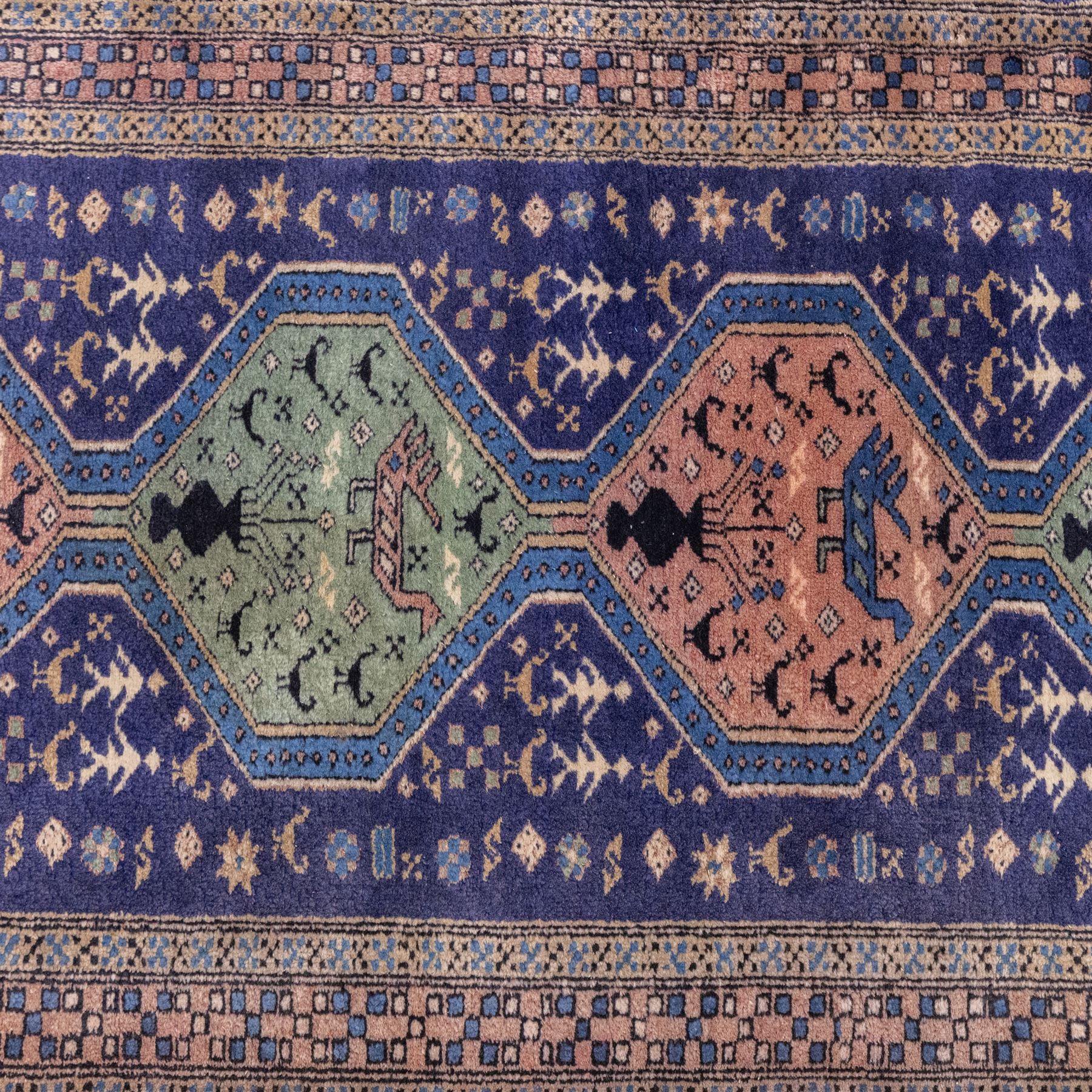 North West Persian Ardebil hand-knotted runner, indigo field composed of a vertical series of large linked hexagonal medallions alternating soft terracotta and sage-green grounds, medallions connected narrow waist panels, surround field filled with geometric devices on a pale blue ground, principal border decorated with a repeating geometric and floral motif on a light ground flanked by narrow guard stripes incorporating small rosettes, with cotton fringe ends 