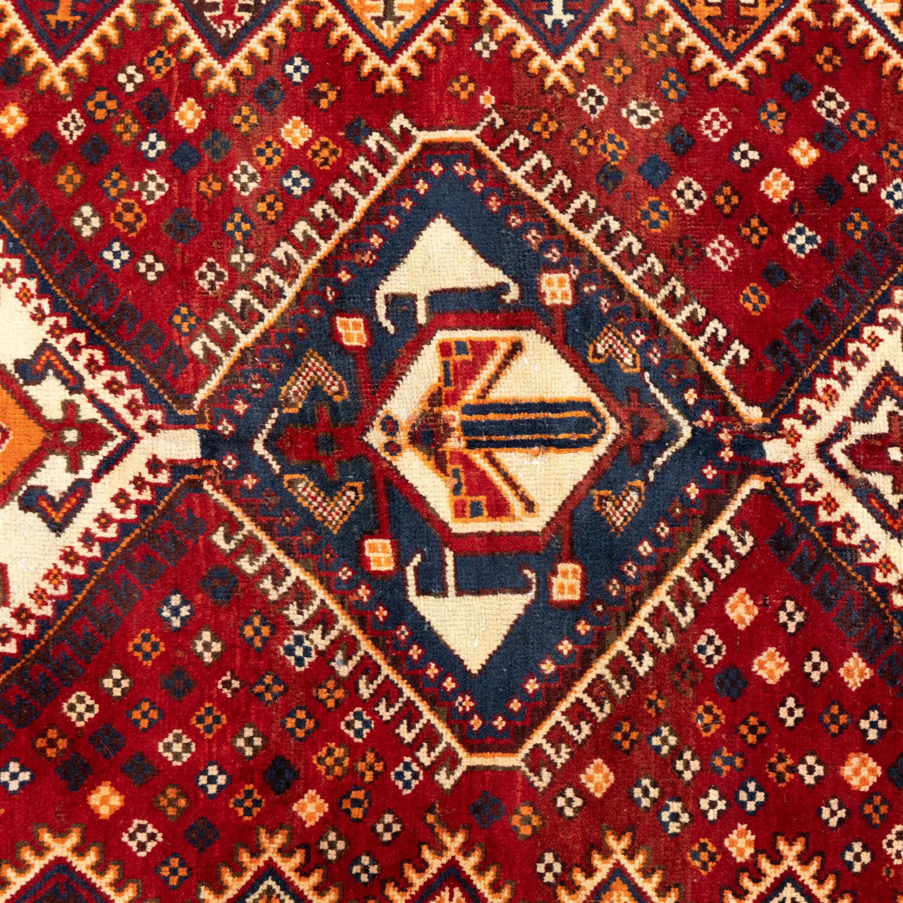 South West Persian Cori hand-knotted rug, red field with three central stepped lozenge medallions enclosing stylized geometric motifs surrounded by scattered rosette devices and angular ornaments within multiple geometric borders, with fringe ends  