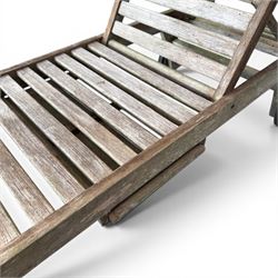Pair of teak garden sun loungers, with slatted adjustable backrests, integrated wheels and sliding pull-out side trays, weathered natural finish.