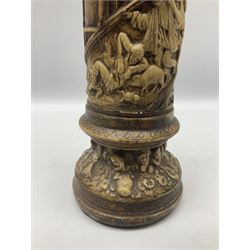 Vase of cylindrical form decorated in relief with spiralled bands of figures with drinks and animals in raucous scenes with alternating bands of classic church style windows, raised upon circular spreading base with faces, H40cm 