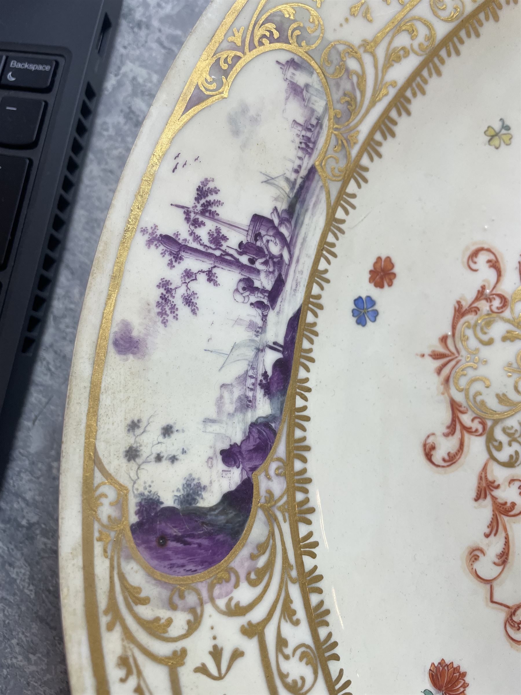 Large and impressive 18th century Meissen dish, finely painted with a chinoiserie scene to a central shaped reserve, depicting figures and attendants engaged in various pursuits, the reserve with gilt scrollwork edge, filled with Böttger lustre and detailed with iron red scrollwork, surrounded by flower heads, the rim with four quatrofoil Kauffahrtei scene panels of merchants and figures by a quayside in purple monochrome, with gilt scroll border, with under glazed blue crossed swords mark, and gilt gilders mark, D39cm
