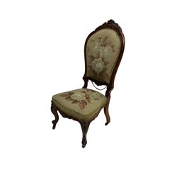 Victorian simulated rosewood framed nursing chair, the cresting rail carved with scrolls and foliage, upholstered in floral needlework cover, on cabriole supports with brass and ceramic castors