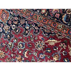 Persian Meshed carpet, plum ground and decorated with stylised flower heads and interlacing foliate, large central stylised medallion with orange detail, the orange mirrored in the five band border decorated with scrolling floral design, signature panel to end 