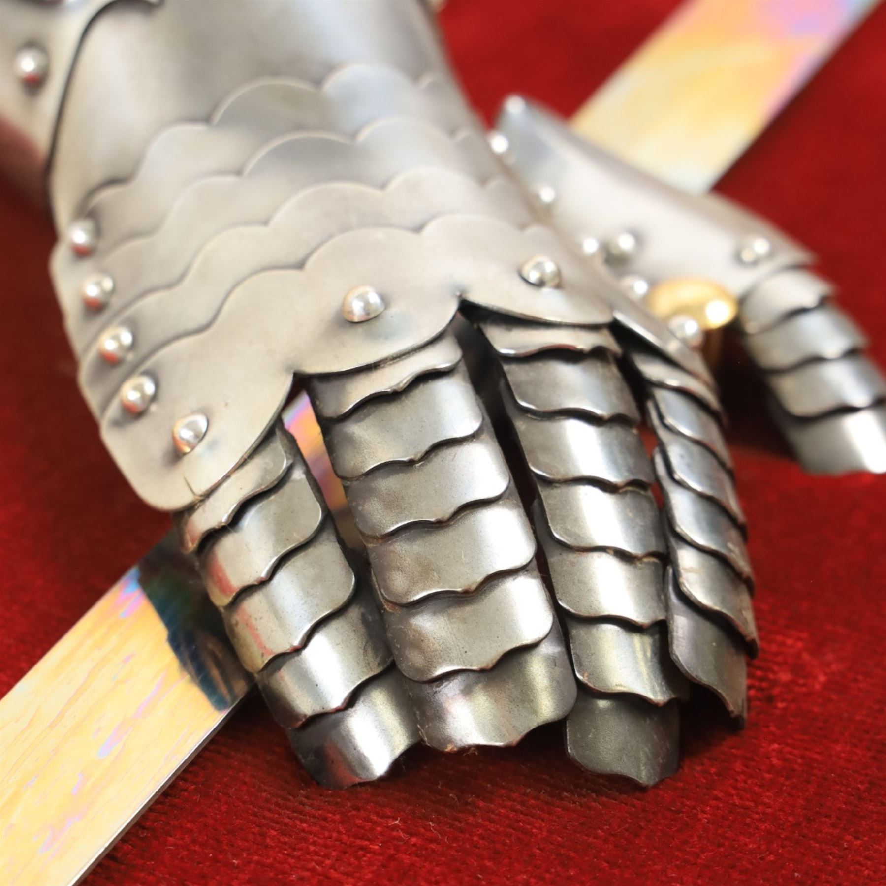 Three replica gauntlets, each housed upon a red wall shield, two with daggers, the third with a sword, largest H102cm