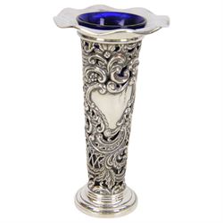 Two late Victorian silver mounted vases, including blue glass mounted example with fluted rim and upon circular foot, hallmarked Henry Matthews, Chester 1900 and a tapering example with fluted rim and pierced embossed scroll decoration to body, with blue glass liner, hallmarked James Deakin & Sons, Chester 1897, tallest H18.5cm