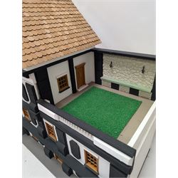 1:24 scale four-storey tudor-style dolls house, with black and white exterior, balcony garden, glazed panelled windows and wooden shingle roof, with decorated interior and wired fireplaces and lighting, H65cm, W58cm, D31cm, 