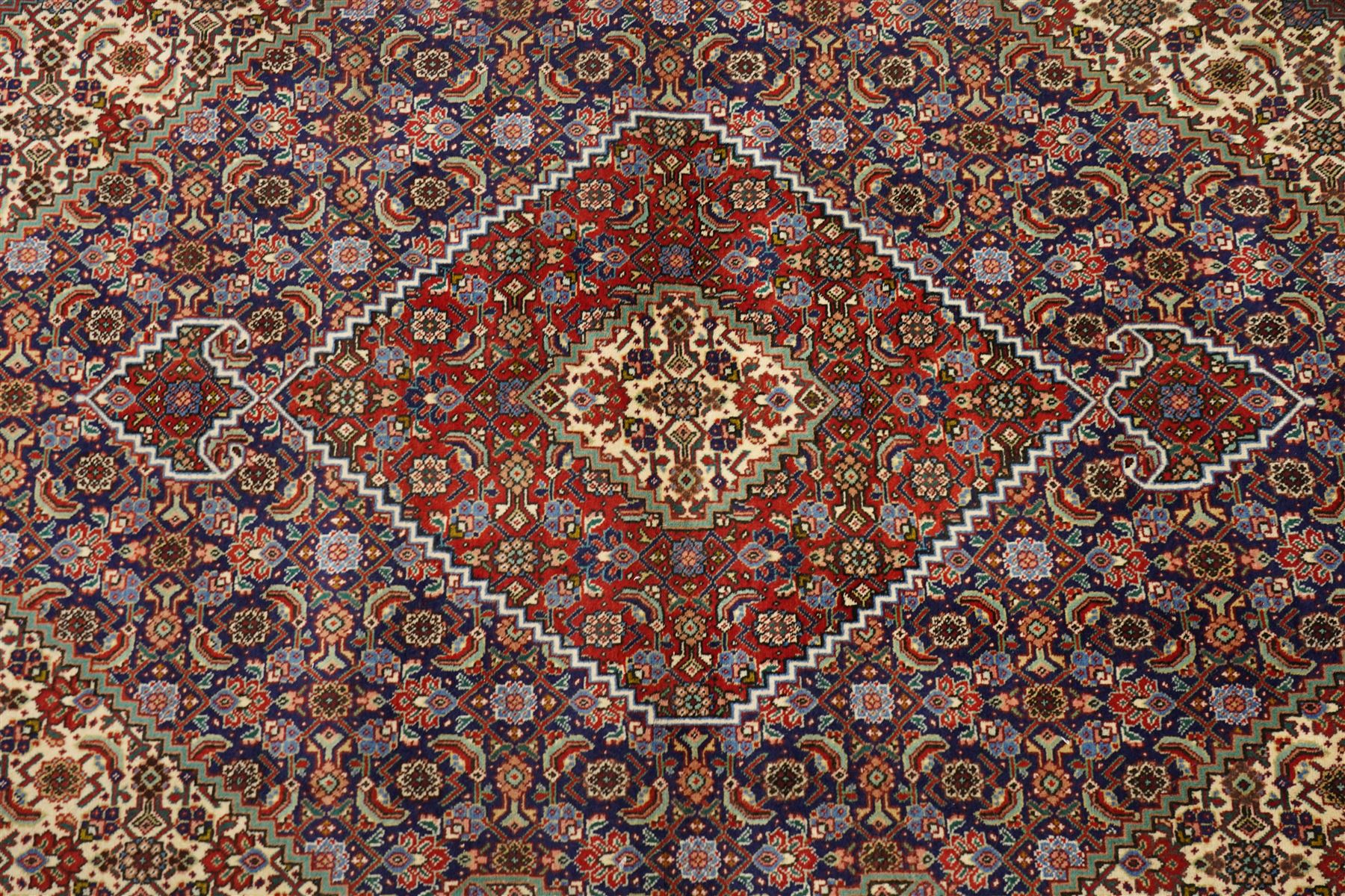 North West Persian Tabriz hand-knotted rug, ivory field with a central lozenge shaped medallion in indigo and madder red, issuing an ornamented arrangement of Herati style motifs, rosettes and angular floral elements, conforming spandrels on an ivory ground, main border in madder red with stylized vinery and palmettes, flanked by multiple guard border, with cotton fringe ends 