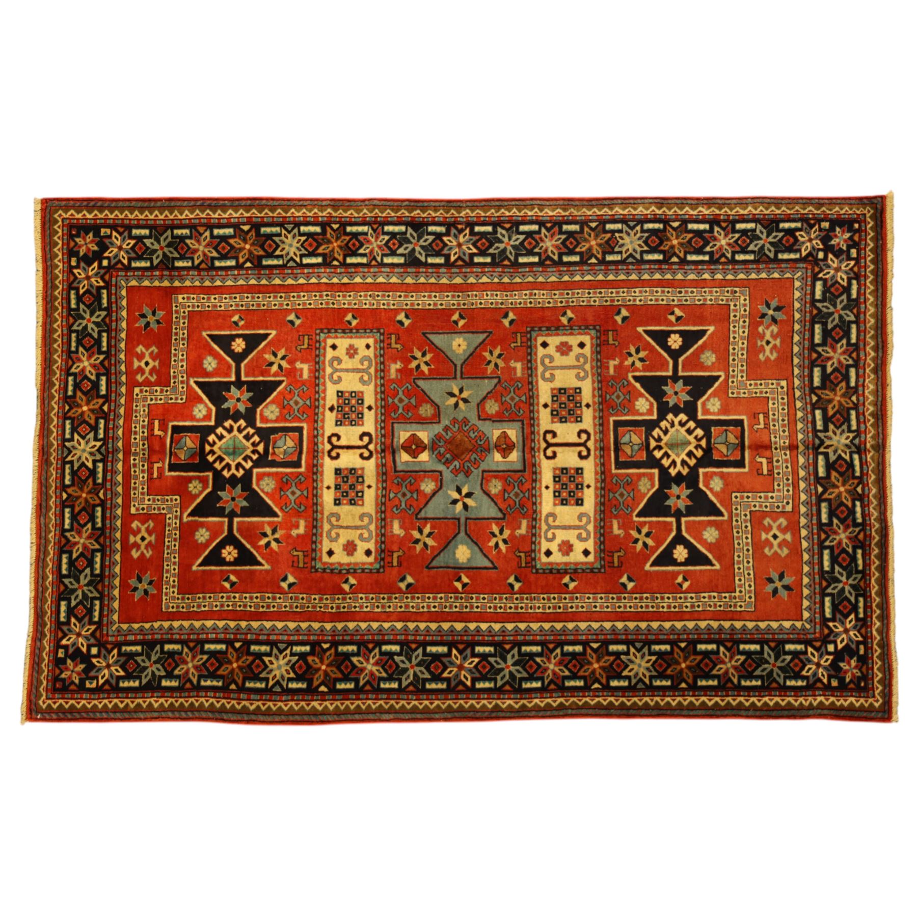 North West Persian Ardebil rug, three-medallion design with central octagonal starburst medallion flanked by two cruciform cartouche-style medallions, main field in terracotta red populated with hooked geometric, zoomorphic shapes and rosettes, main border with a series of eight pointed stars in alternating tones on a dark navy ground, separated by small diamonds and geometric fillers, inner and outer guard stripes with a classic reciprocal sawtooth motif 