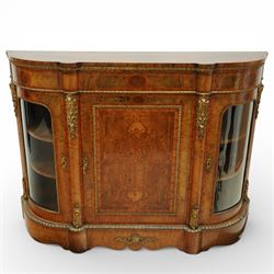 Late Victorian figured walnut credenza, the shaped demi-lune top with cross-banding and stringing over an inlaid frieze with foliate gilt-metal mounts, fitted with a central geometric-inlaid panelled door, flanked by convex-glazed side-cabinets with a gilt metal slip and outer-banding, the uprights surmounted by gilt-metal cartouche mounts with cascading foliage details, raised on a shaped skirted base with central female-mask gilt mount
