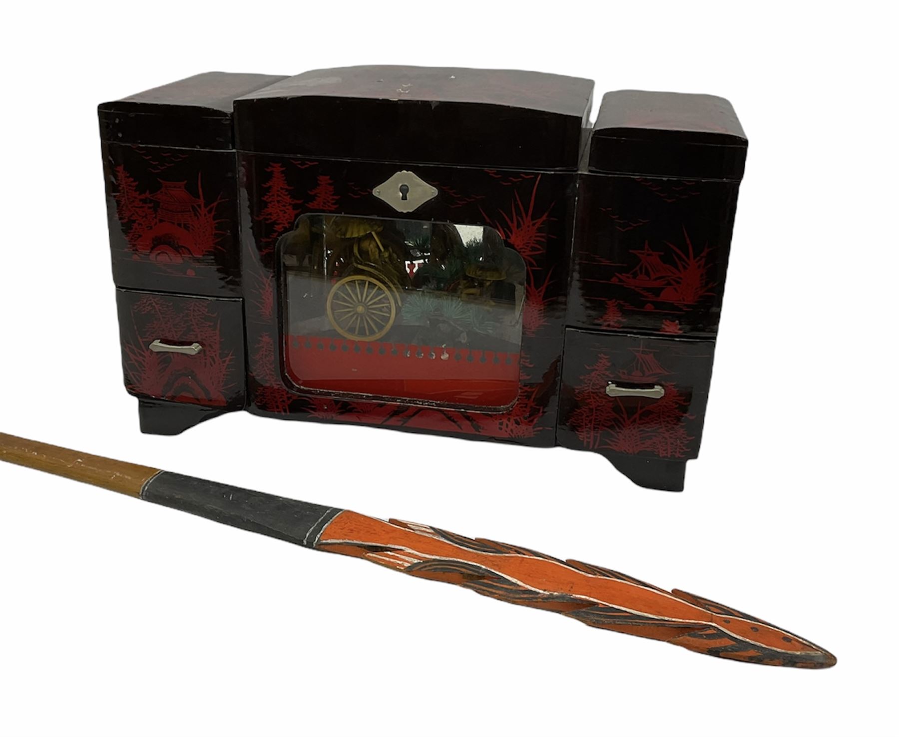 Oriental lacquered jewellery box, the body decorated with a black and red mountainous riverscape enclosing a glass compartment with simulated ivory rickshaw figure and three hinged lids opening to reveal mirror and various compartments and painted ceremonial stick