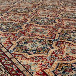 Central Persian Kirman carpet, the field arranged with alternating indigo star shaped and red cruciform compartments, each filled with rosettes, flowerheads and scrolling foliage, enclosed by a broad ivory palmette border and red floral guard bands