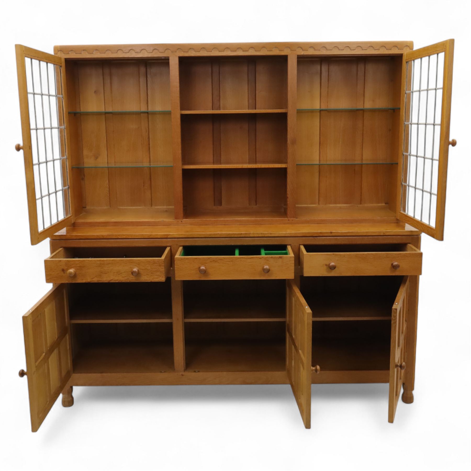 David 'Oakleafman' Langstaff - oak three drawer dresser, the scalloped cornice above a back with central open shelves flanked by two glazed and leaded cupboard doors opening to glass shelves, upon a base with adzed top carved with signature leaf, three drawers and three panelled cupboard doors with turned handles, upon octagonal feet, from the workshop of David Langstaff, Easingwold, Yorkshire