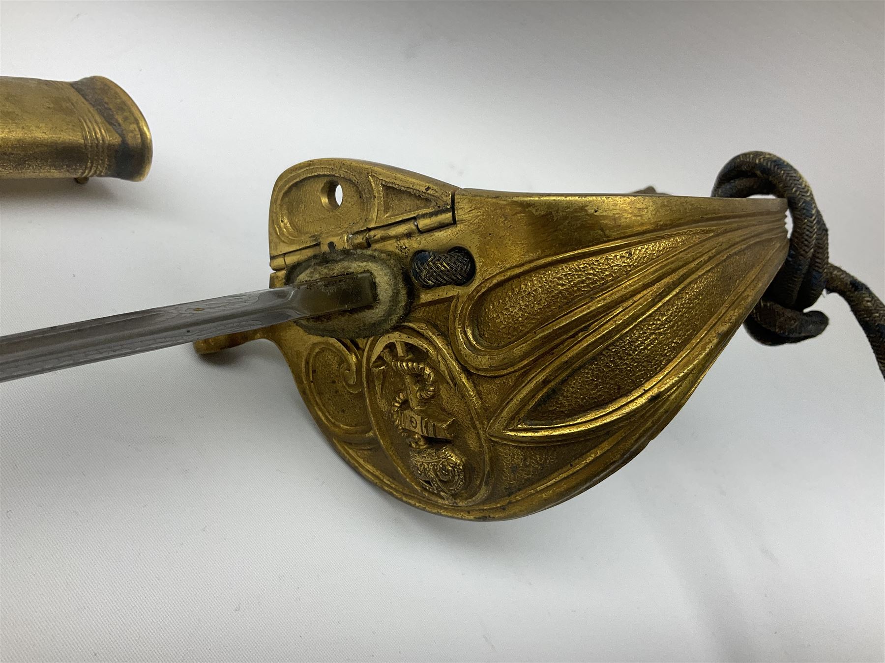 WW1 George V era 1827 Pattern Royal Naval Officer’s sword, the 80cm fullered steel blade decorated with crown, fouled anchor etc and marked Gieves Portsmouth London Edinburgh Devonport to the ricasso, gilded hilt with fouled anchor and crown, wire-bound ray skin grip, lion’s head pommel with mane backstrap, folding/locking langet and full bullion knot; in  leather scabbard having twin brass lockets with hand engraved panels and twin suspension rings L94cm overall. Provenance: By direct family descent from Brian Heathcote HMS Conqueror later Superintendant in the Liverpool Special Constabulary.