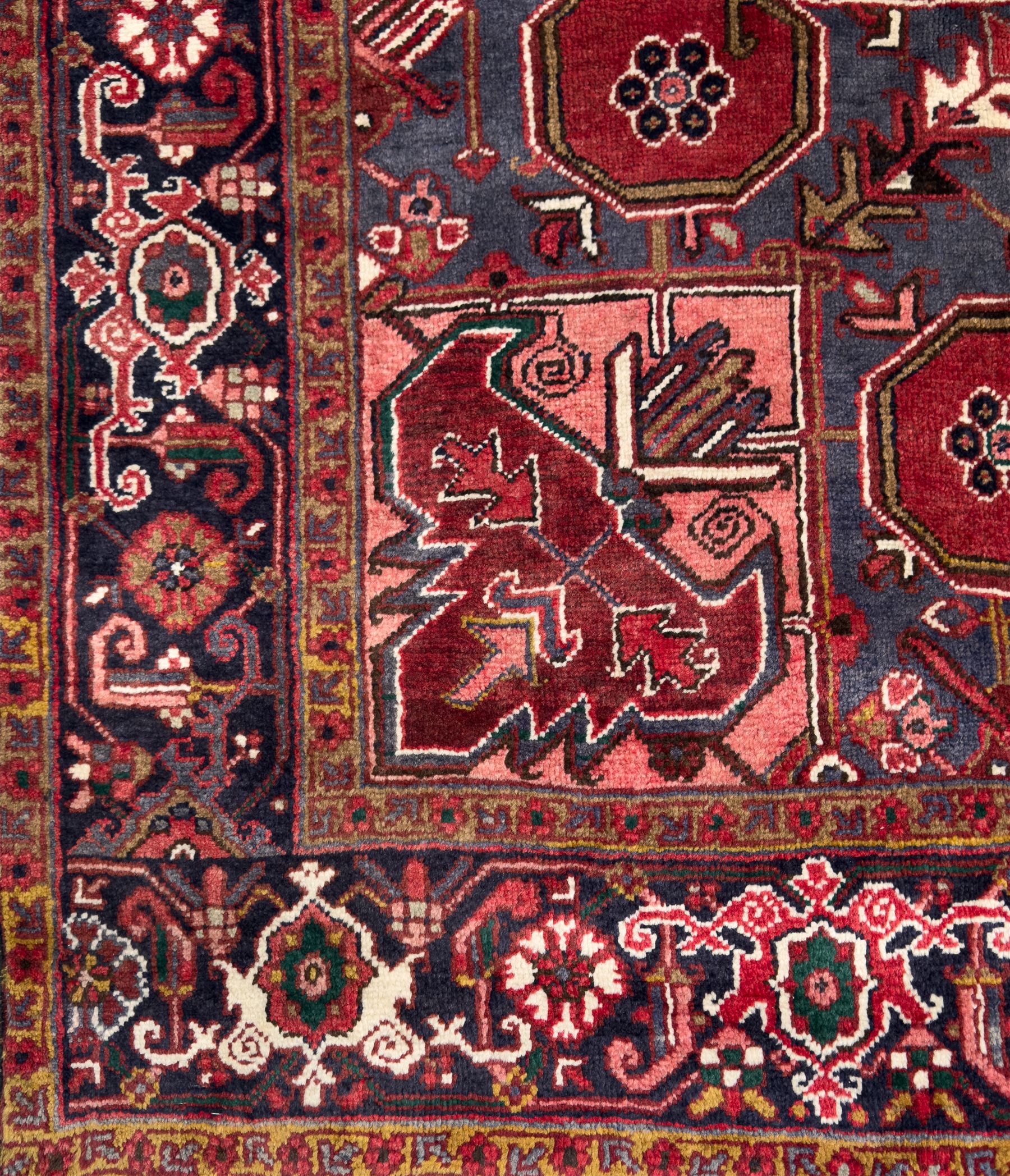 Northwestern Persian Heriz hand-knotted carpet, madder red field with a bold stepped medallion in indigo, ivory, and ivory, surrounded by angular floral motifs and stylized leaves, and the spandrels set within a dark border of rosettes and angular vine motifs, 335cmx252cm