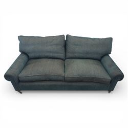 Late 20th century three seat sofa upholstered in green fabric, with gently rounded scroll arms, loose seat and back cushions, raised on turned wooden legs with castors, rear splayed legs