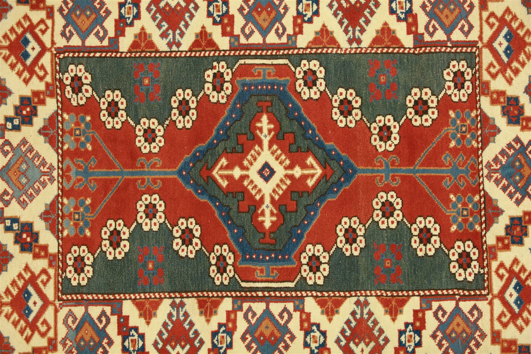 Caucasian Soumak rug, red madder field and teal panels, with bold stepped diamond medallion with hooked motifs and cruciform devices, and floral rosette clusters, surrounded by an ivory border with large hooked diamonds and stylized ram's horn devices, flanked by narrow guard stripes





