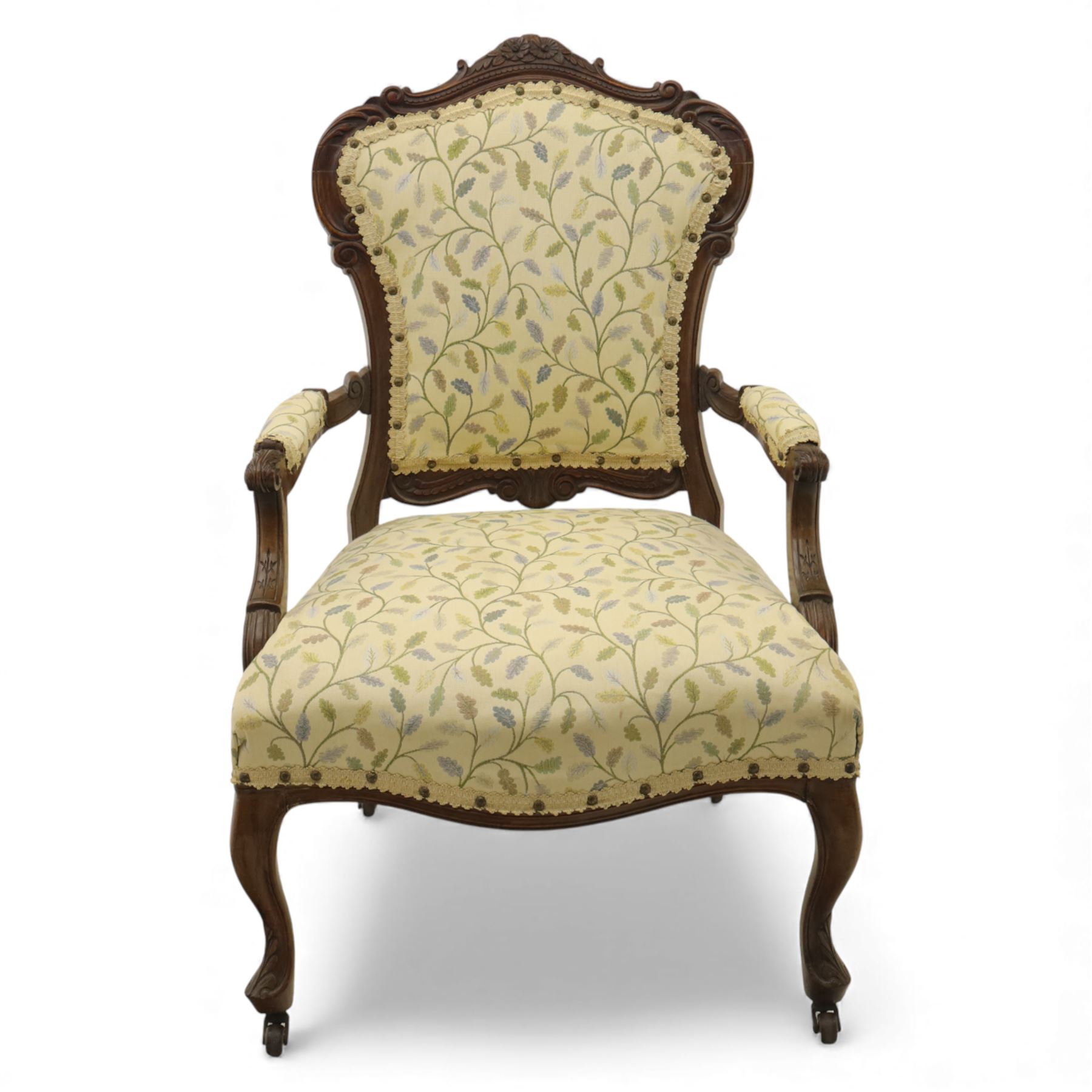 Victorian mahogany framed upholstered armchair, shaped and scroll carved cresting rail above a padded upholstered back with applied braid trim, swept open arms with carved terminals and upholstered arm pads, over a serpentine fronted deep stuffed seat, raised on cabriole forelegs terminating in carved claw feet