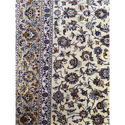 Central Persian Kashan hand-knotted carpet, ivory field with an all-over design of scrolling vines, lotus palmettes, and rosettes in shades of blue, gold, and brown within a blue ground border of palmettes and arabesques between multiple guard stripes