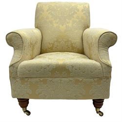 Traditionally shaped hardwood-framed armchair, rolled back and arms, upholstered in pale gold and cream damask fabric with repeating foliate pattern, on turned feet with brass cups and castors