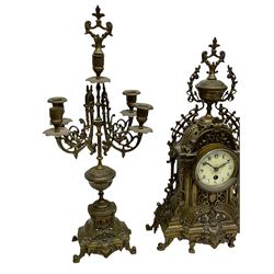 A late 19th century profusely decorated brass cased timepiece mantle clock with two matching five light candelabra, break front case raised on cast feet with decorative scroll work and a shaped urn to the pediment, eight-day spring driven French timepiece movement with an enamel dial, steel fleur di Lis hands, Roman numerals and minute track, egg and dart slip within a flat glazed bezel. With Pendulum.

