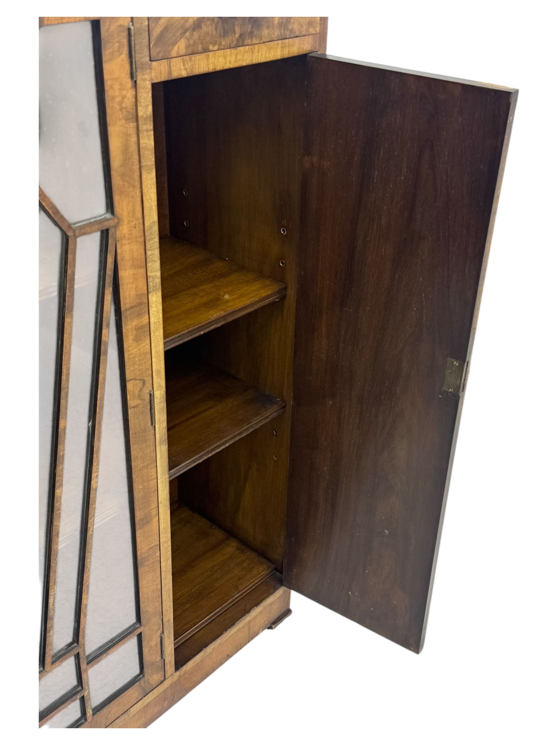 Art Deco burr walnut drinks cabinet, geometric central glazed astragal door enclosing two fixed shelves, flanked by symmetrical bookmatched veneered cupboards with drawers above 
